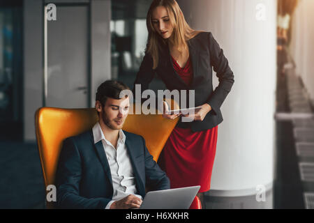 Gruppe von Geschäftsleuten in modernen zeitgenössischen Büroeinrichtung, ein Mann mit gelben Sessel zeigt etwas auf laptop Stockfoto