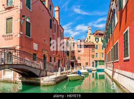 Boote auf schmalen Kanal zwischen bunten Häusern unter blauem Himmel in Venedig, Italien. Stockfoto