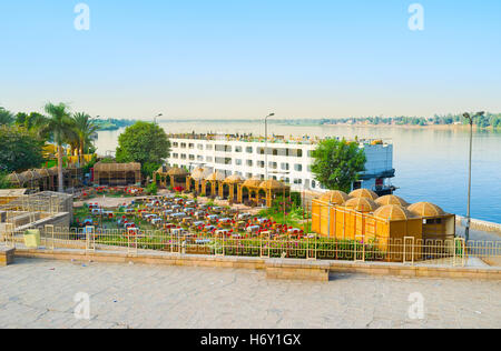 Das Kreuzfahrtschiff am Ufer des Nils in Kom Ombo mit dem Blick auf Luxusrestaurant-Komplex, umgeben von Grün, Ägypten. Stockfoto