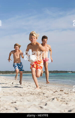 Junge läuft mit Rugby-Ball gejagt von Bruder und Vater am Strand, Mallorca, Spanien Stockfoto