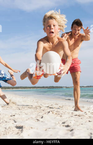 Junge, springen Luft mit Rugby-Ball gejagt von Bruder und Vater am Strand, Mallorca, Spanien Stockfoto