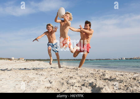 Junge, springen mit Rugby-Ball gejagt von Bruder und Vater am Strand, Mallorca, Spanien Stockfoto