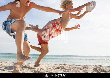 Junge und Vater laufen zur Erreichung Bruder mit Rugby-Ball am Strand, Mallorca, Spanien Stockfoto