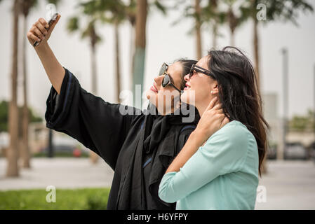 Junge Naher Osten Frau tragen traditionelle Kleidung unter Smartphone Selfie mit Freundin, Dubai, Vereinigte Arabische Emirate Stockfoto