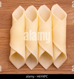 Cheelse Scheiben fein säuberlich aufgerollt auf eine Holzoberfläche. Stockfoto