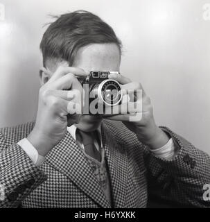 1950, historische, England, UK, jungen Mann, der eine Jacke mit Krawatte, die ein in der Hand gehaltenes Bild mit einem italienischen gemacht Sucher film Kamera, Ferrania ibis Primar 75. Stockfoto