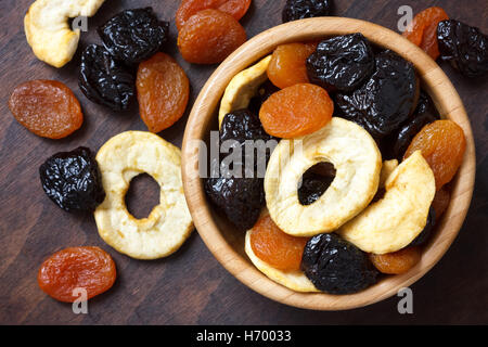 Gemischte Trockenfrüchte in einer hölzernen Schüssel und auf der dunklen Oberfläche des Holzes. Von oben. Stockfoto