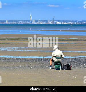 Älterer Mann sitzt allein auf Ryde Isle Of Wight UK Strand bei Ebbe skizzieren einen Blick auf den Solent in Richtung fernen Portsmouth an heißen Sommertag blauer Himmel Stockfoto