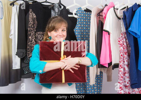 Fröhliches junges Mädchen hat ein Willkommensgeschenk im Hintergrund hängen Dinge auf Kleiderbügeln erhalten. Stockfoto