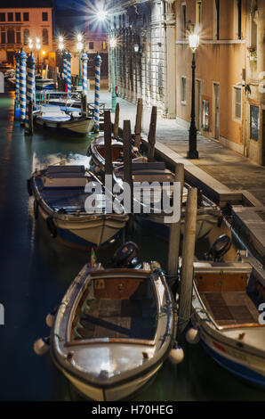 Verankerte Boote in Venedig Canal, leere Straße beleuchtet von Lampen, Blick von einer Brücke. Stockfoto