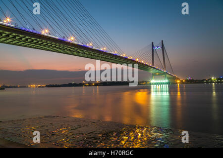 Vidyasagar Brücke (Setu) am Fluss Ganges in der Dämmerung mit Stadt leuchtet Reflexionen. Stockfoto