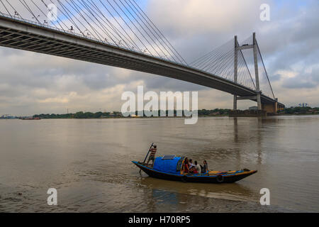 Hölzerne Land Bootsfahrt auf dem Fluss Ganges an einem bewölkten Tag mit Vidyasagar Setu (Brücke) auf dem Hintergrund. Stockfoto