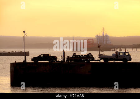 Fischer auf dem Kai in Milford Haven mit einem Öltanker im Hintergrund einen Fang anlanden. Stockfoto