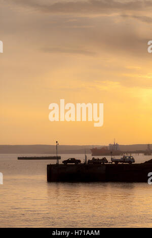 Fischer auf dem Kai in Milford Haven mit einem Öltanker im Hintergrund einen Fang anlanden. Stockfoto