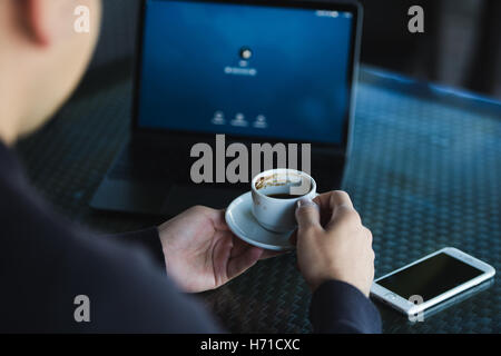 Frischer Kaffee für große Ideen. Ansicht von oben Mann am Laptop arbeiten und halten Tasse Kaffee im Café sitzend Stockfoto