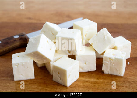 Quadratische Würfel Feta Käse isoliert auf Holzbrett mit Messer. Stockfoto