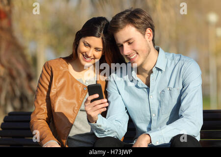 Paar gerade ein smart Phone sitzen auf einer Bank Stockfoto