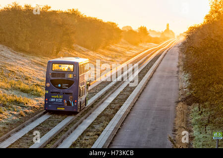 Über, Cambridgeshire UK, 2. November 2016.  Eine geführte Bus-Köpfe in Richtung Cambridge als die Sonne steigt über die Gleise auf eine klare, gestochen scharfe, frostigen Herbstmorgen. Die klare Luft und die ersten Frost im Herbst dieses Jahres in den Osten des Vereinigten Königreichs Schuppen einen goldenen Schimmer auf die Morgen pendeln. Kredit Julian Eales/Alamy Live-Nachrichten Stockfoto