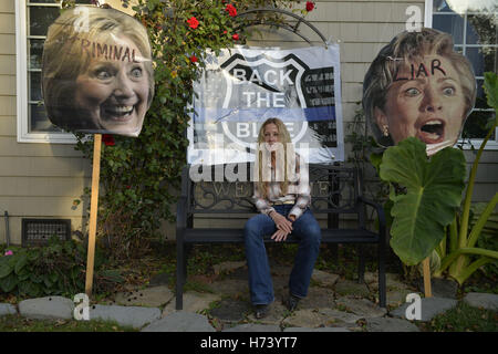 Bellmore, New York, USA. 2. November 2016. EILEEN FUSCALDO, ein starker Donald Trump Befürworter, sitzt in ihrem Vorgarten auf eine Sitzbank mit großen Bildern von Hillary Clintons Kopf auf Stöcke und '' zurück the Blue'' Polizei Abzeichen Zeichen hinter ihr, einige von vielen in ihrem Vorgarten für den republikanischen Präsidentschaftskandidaten, D. J. Trump, und gegen demokratische eins, H. R. Clinton. Bildnachweis: Ann Parry/ZUMA Draht/Alamy Live-Nachrichten Stockfoto