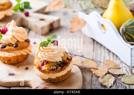 Hausgemachte Herbst Cranberry Kürbis Muffins mit Frischkäse-Glasur auf rustikalen Holztisch Stockfoto