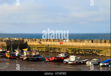 Boote auf dem Schlamm bei Ebbe, geschützt von der Hafenmauer in Staithes in England Stockfoto