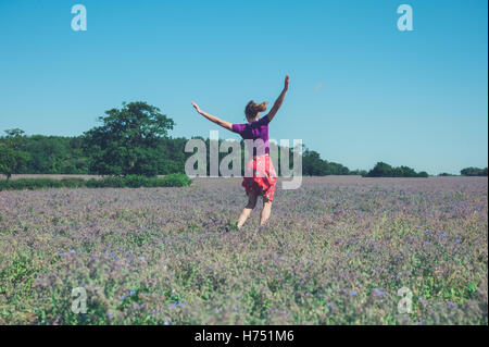 Eine glückliche junge Frau ist um in einem Feld von lila Blüten an einem sonnigen Sommertag springen. Stockfoto