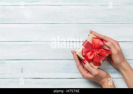 Weibliche Hände halten Weihnachten oder Valentinstag Geschenk oben Holztisch. Draufsicht mit Textfreiraum Stockfoto