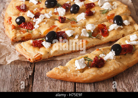 In Scheiben geschnitten italienische Focaccia mit getrockneten Tomaten, Feta und Oliven auf den Tisch. Closeup horizontale Stockfoto