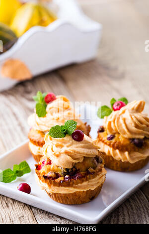 Hausgemachte Herbst Cranberry Kürbis Muffins mit Frischkäse-Glasur auf rustikalen Holztisch Stockfoto