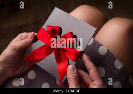 Nahaufnahme von den Händen einer Frau mit Polka Kleid hielt eine schwarze Karte mit rotem Band über Knie Stockfoto