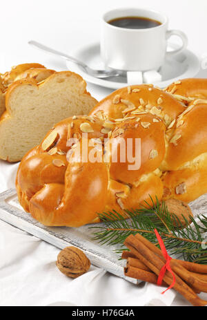 ganze und geschnittene süßes Brot mit Mandeln und Rosinen auf Holzbrett und weiße Serviette geflochten Stockfoto