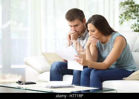 Besorgt paar lesen eine wichtige Benachrichtigung in einem Brief sitzen auf einer Couch im Wohnzimmer zu Hause Stockfoto