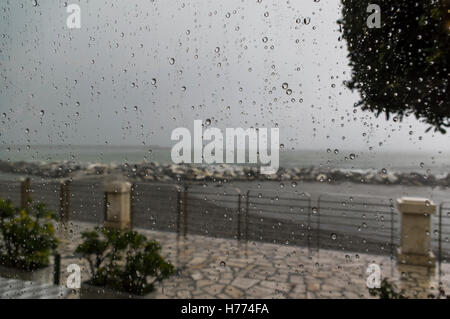 Regentropfen auf einem Fenster während eines Gewitters. Meer und Mittelmeer als Fokus-Hintergrund. Stockfoto