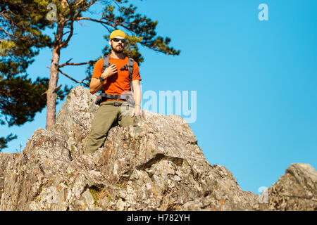 Junger Mann mit Bart ist durch den Berg, touristische Rucksack steht auf Rock Hill genießen Natur Blick, Reisen Sommerferien in Bergen Stockfoto