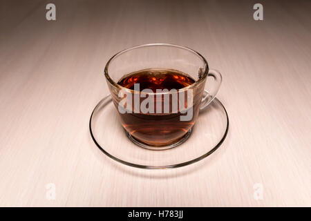 transparente Glas-Tasse mit Tee auf eine Untertasse auf einen Tisch gestellt Stockfoto