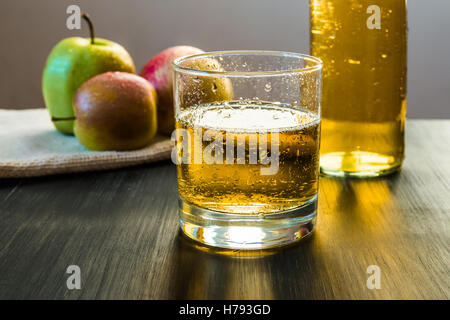 Apfelwein in ein Glas vor Äpfeln auf rustikalen Holztisch Stockfoto