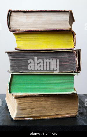 Stapel von alten Vintage Bücher in verschiedenen Farben auf schwarzer Holztisch vor hellen Innenräumen Hintergrund in natürlichem Licht. Stockfoto