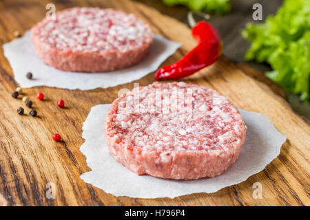 Rohe frische Burger Frikadellen auf Schneidbrett aus Holz Stockfoto