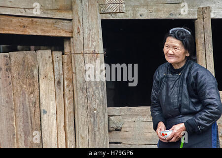 Eine alte Frau geht mit einer Tasse in einem Dorf westlich von Zhaoxing, in der Provinz Guizhou, China Stockfoto