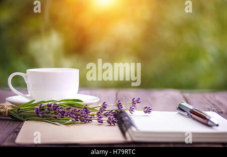 leere weiße Notebook, Blumen und Kaffee auf dem Schreibtisch im Freien im Sommer Stockfoto