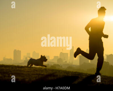 Unschärfe Silhouetten von Jogger und seinem Hund laufen vor der Skyline der Stadt von goldenen Sonnenaufgang in London Stockfoto