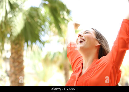 Porträt einer begeistert Frau mit Augen geschlossen heben Arme zum Himmel Natur mit Palmen im Hintergrund Stockfoto
