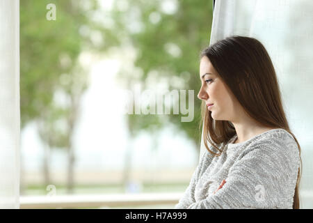 Profilbildnis einer Sehnsucht Frau im freien Blick durch ein Fenster zu Hause oder im Hotelzimmer mit einem grünen Hintergrund Stockfoto