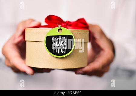 Closeup von einem kaukasischen Jüngling in einem weißen Hemd hält eine Geschenkbox mit einem Label gebunden und den Text gerne schwarzen Freitag wri Stockfoto