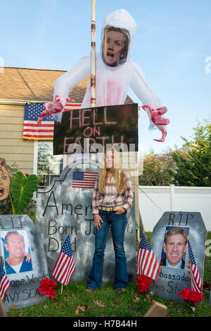 Bellmore, Vereinigte Staaten von Amerika. 2. November 2016. Bellmore, New York, USA. 2. November 2016. EILEEN FUSCALDO, Donald Trump Unterstützer, steht in einem Friedhof Display in ihrem Halloween Vorgarten Display mit einem großen Hillary Clinton Geist mit "Hölle auf Erden" Schild drohend über Fuscaldo Kopf und Grabsteine mit Fotos der Amerikaner in Bengasi getötet. Ihr Hof Halloweendekoration hatte viele Schilder und Disaplys zur Unterstützung der republikanische Präsidentschafts Kandidat D. J. Trump und gegen demokratische H. R. Clinton. Bildnachweis: Ann E Parry/Alamy Live-Nachrichten Stockfoto