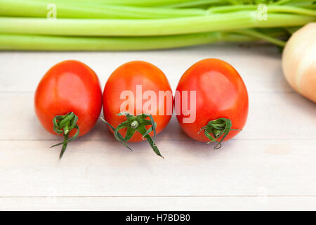 Drei Tomaten umgeben von frischem Gemüse (Zwiebel, Gurke, Salat und Sellerie Blätter) auf Holzbrett Stockfoto