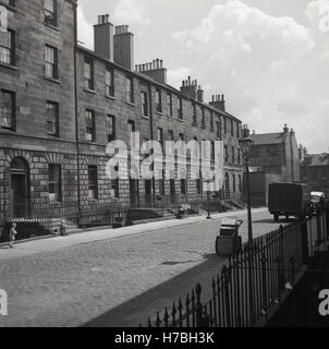 1950er-Jahren, historische, A gepflasterten Straße des späten georgischen terrassierten Gehäuse mit Kellern unter Edinburgh Schloß, Edinburgh, Schottland. Beachten Sie die leeren Kinderwagen auf dem Bürgersteig. Stockfoto