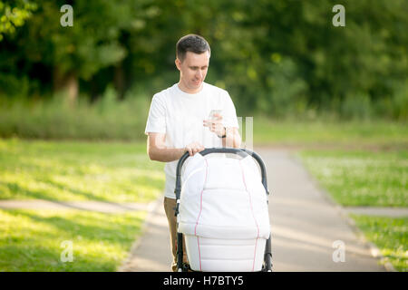 Mann mit Kinderwagen im Park Blick auf Handy-Bildschirm Stockfoto