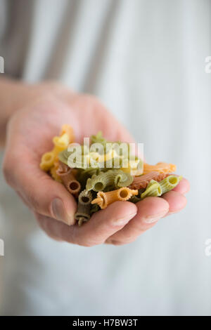 Bunte Nudeln in Nahaufnahme. Hand der Küchenchef hält ungekochte Teigwaren in verschiedenen Farben. Stockfoto