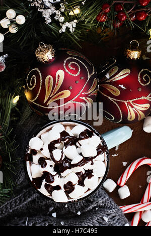 Emaille Tasse heißen Kakao zu Weihnachten mit Marshmallows und garniert mit Schokoladensauce.  Umgeben von einem Schal und Süßigkeiten, Stockfoto